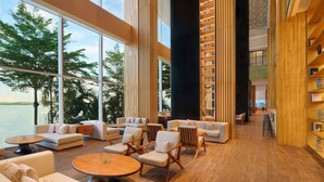 A spacious lobby with high ceilings, large windows offering a view of the water, and a modern interior design featuring wooden accents and comfortable seating areas.