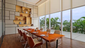 A modern conference room with a long wooden table, beige chairs, and a built-in bookshelf with decorative items.