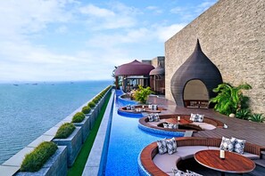 A luxurious outdoor pool area with tiered seating and a view of the sea. - Batam Marriott Hotel Harbour Bay (Batam)