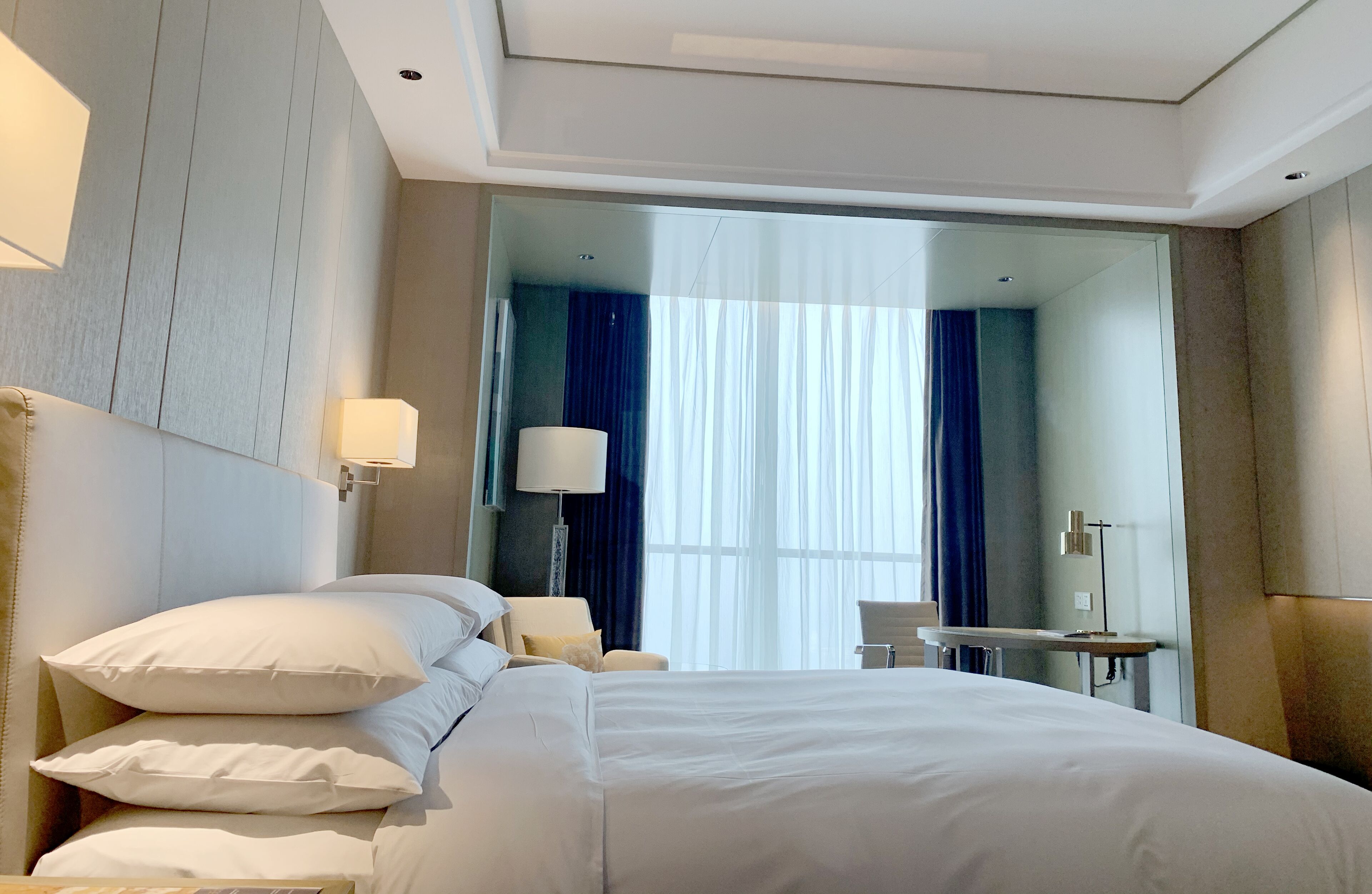 A hotel room with a large bed, a desk, a chair, and a mirror.