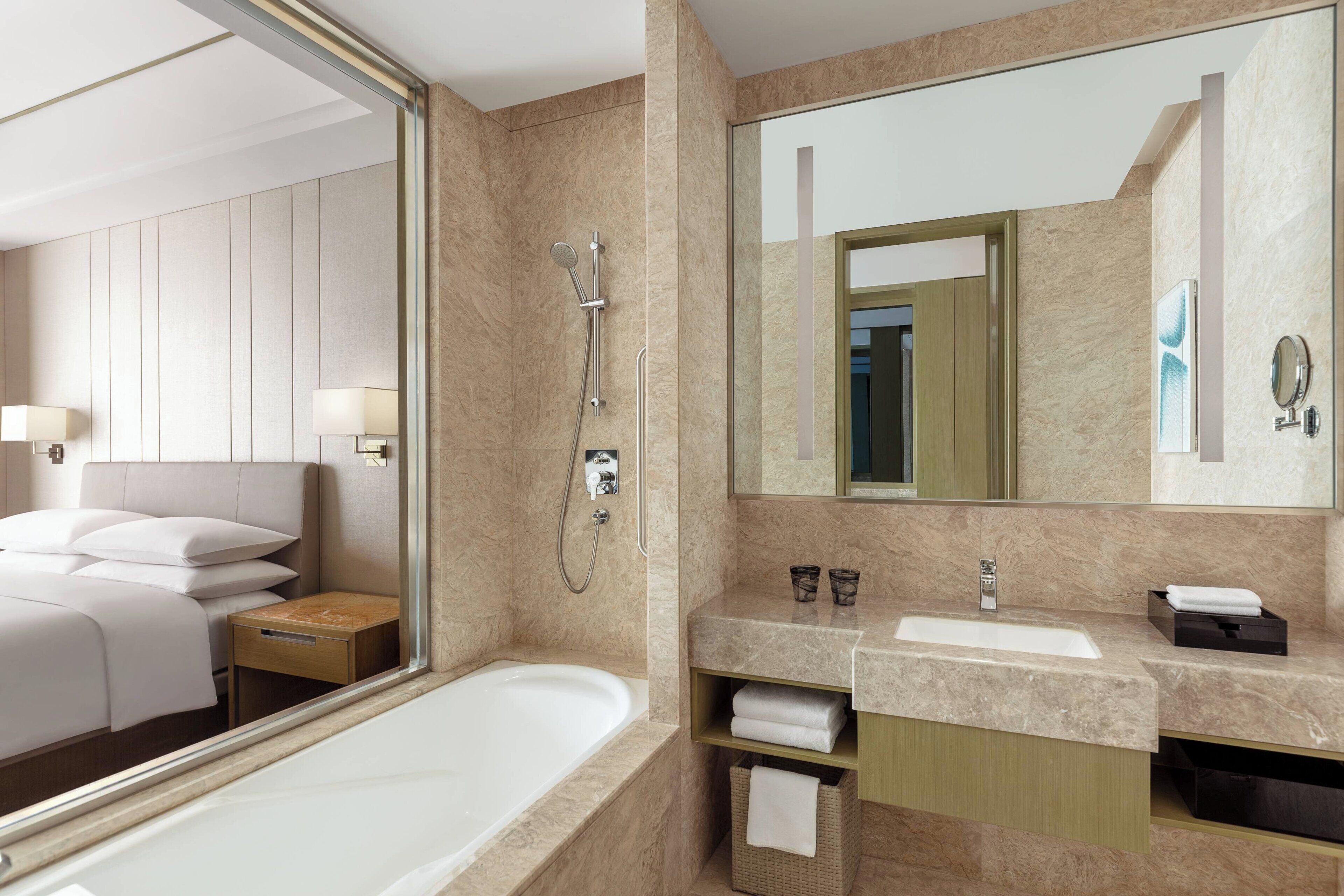 A modern hotel bathroom with a large mirror, a bathtub, a vanity with a sink, and a shower area.
