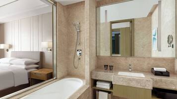 A modern hotel bathroom with a large mirror, a bathtub, a vanity with a sink, and a shower area.