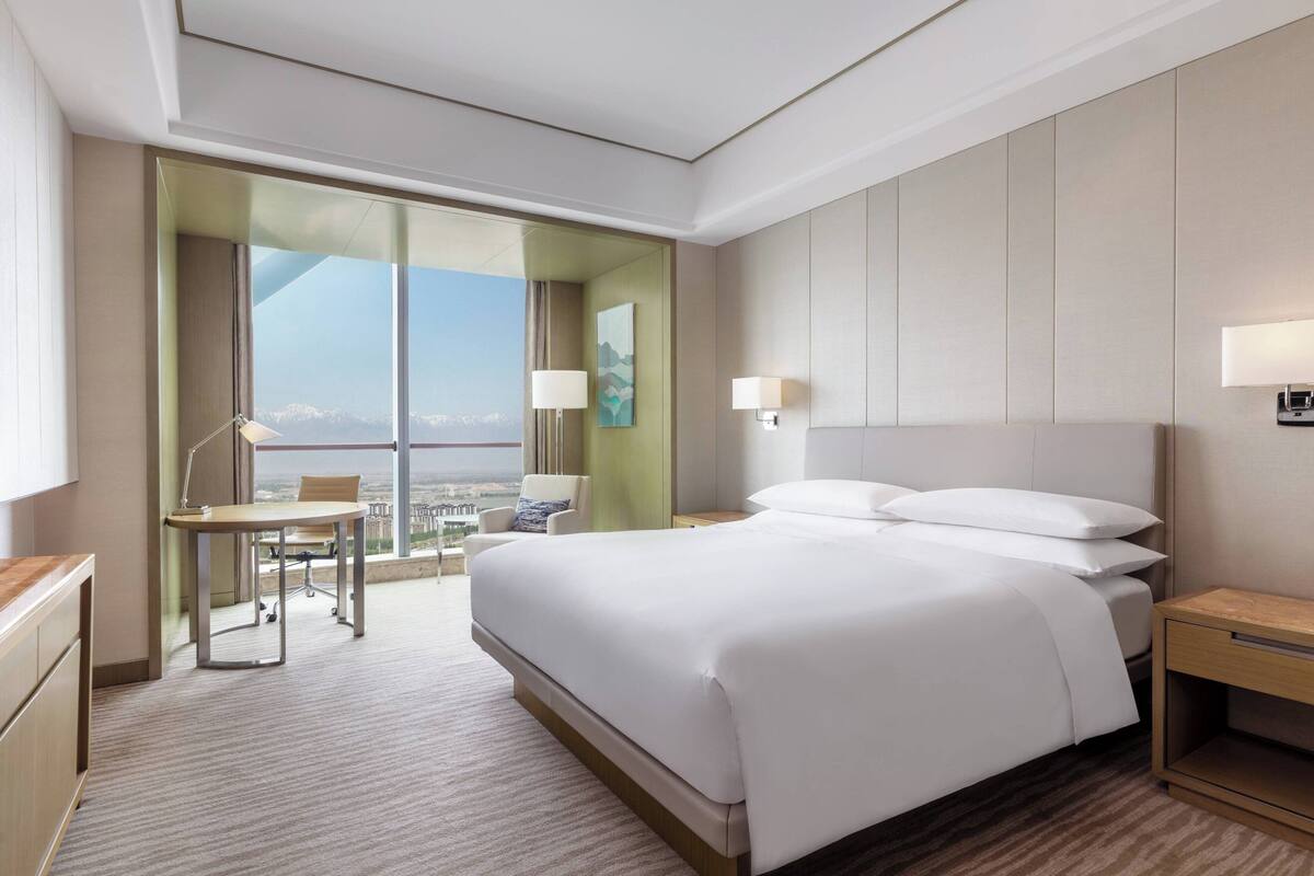 A modern hotel room with a large bed, a desk, and a view of the city.