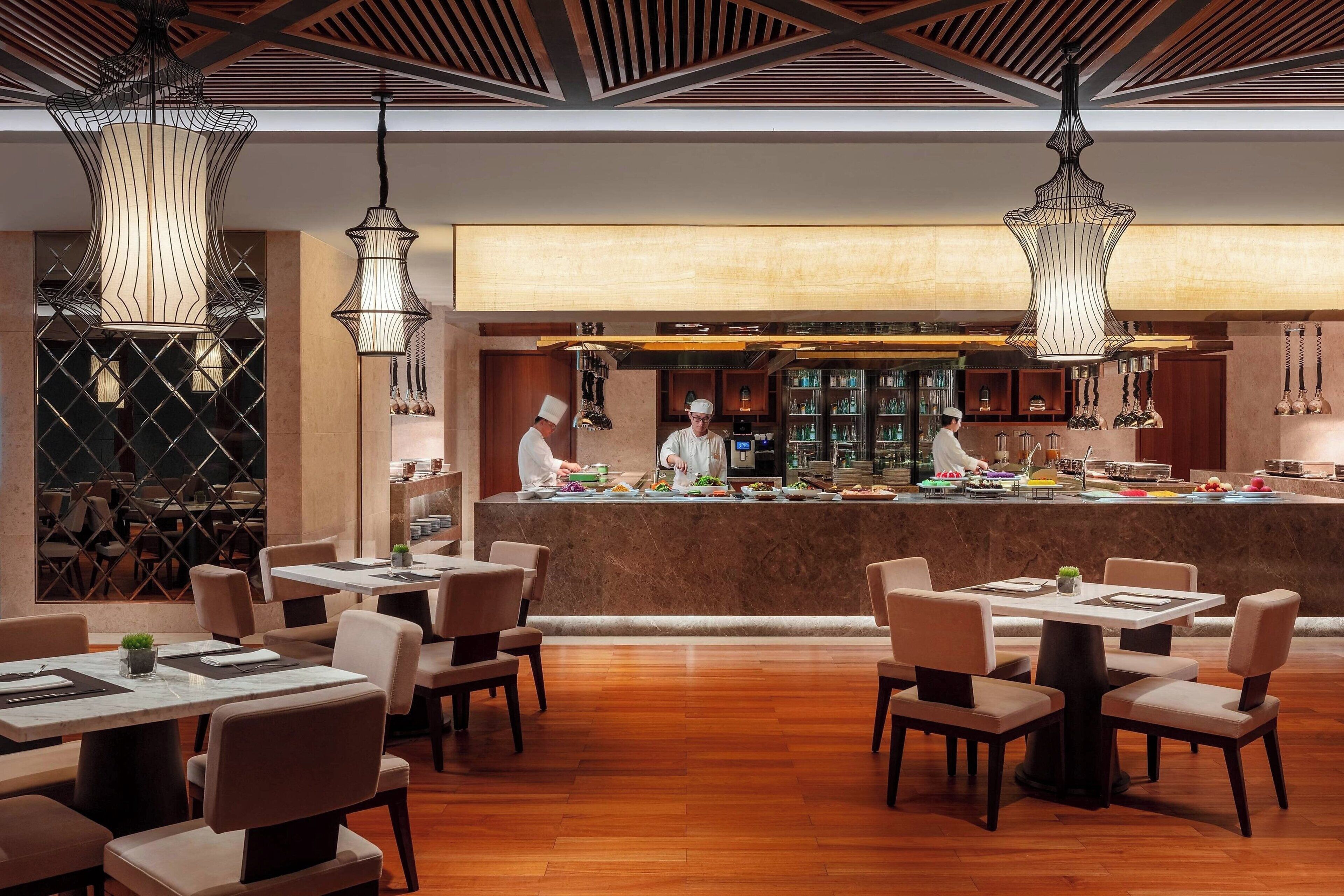 A restaurant with a central bar area, multiple tables, and hanging pendant lights.