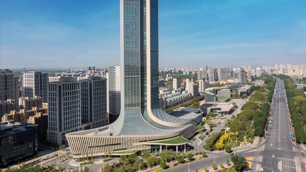 Un edificio moderno de gran altura con fachada curva, rodeado de otros edificios altos y un cielo despejado.
