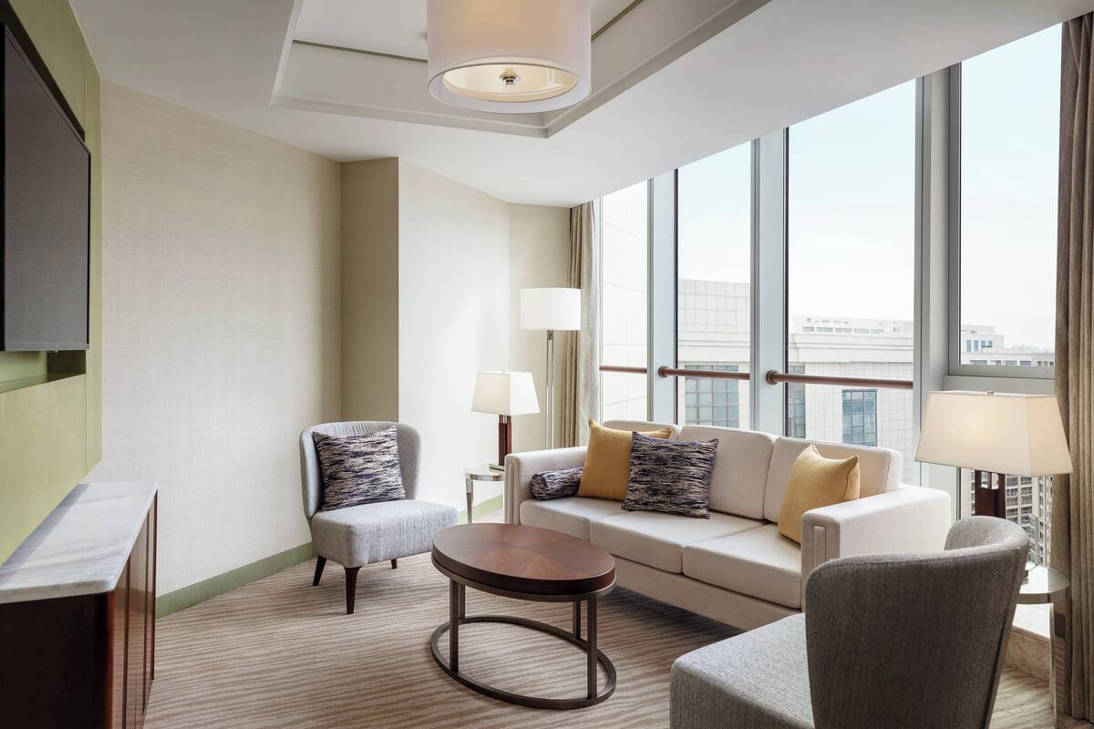 A modern hotel room with a sofa, armchairs, a small table, and a TV.