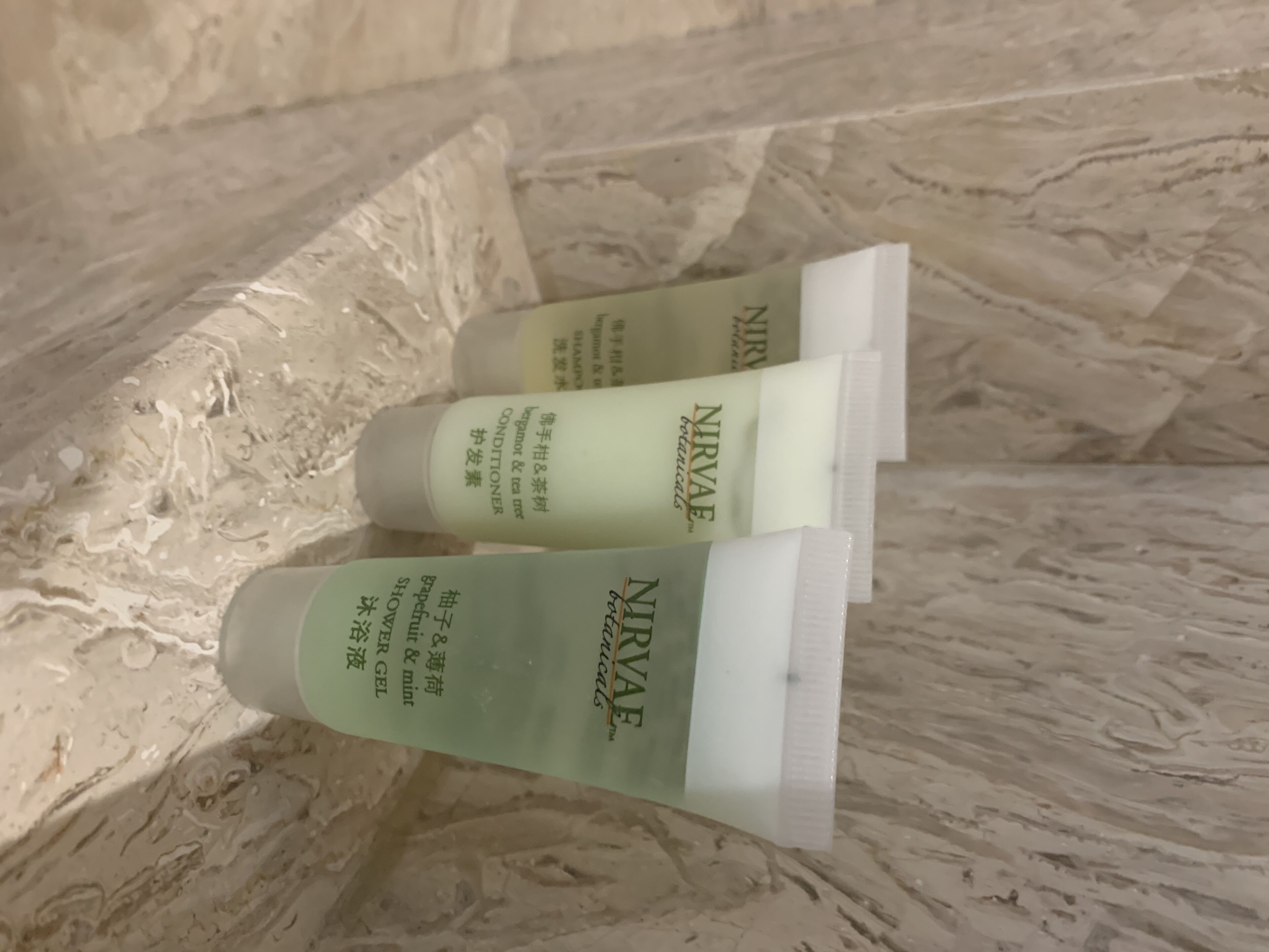 Three bottles of NIRVAE botanical conditioner on a textured surface.