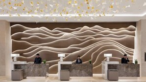 Un área de recepción moderna con tres mostradores, un diseño de pared ondulado y decoraciones florales colgantes.