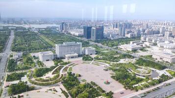 An aerial view of a cityscape with a large central plaza surrounded by modern buildings, roads, and greenery.