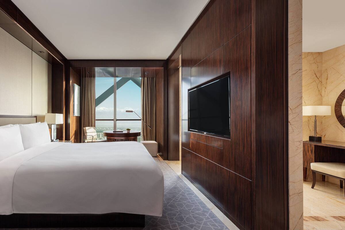 Une chambre d’hôtel dotée d’un grand lit, d’un téléviseur fixé au mur, d’un coin salon avec une table et des chaises, et offrant une vue sur l’extérieur grâce à une grande fenêtre.