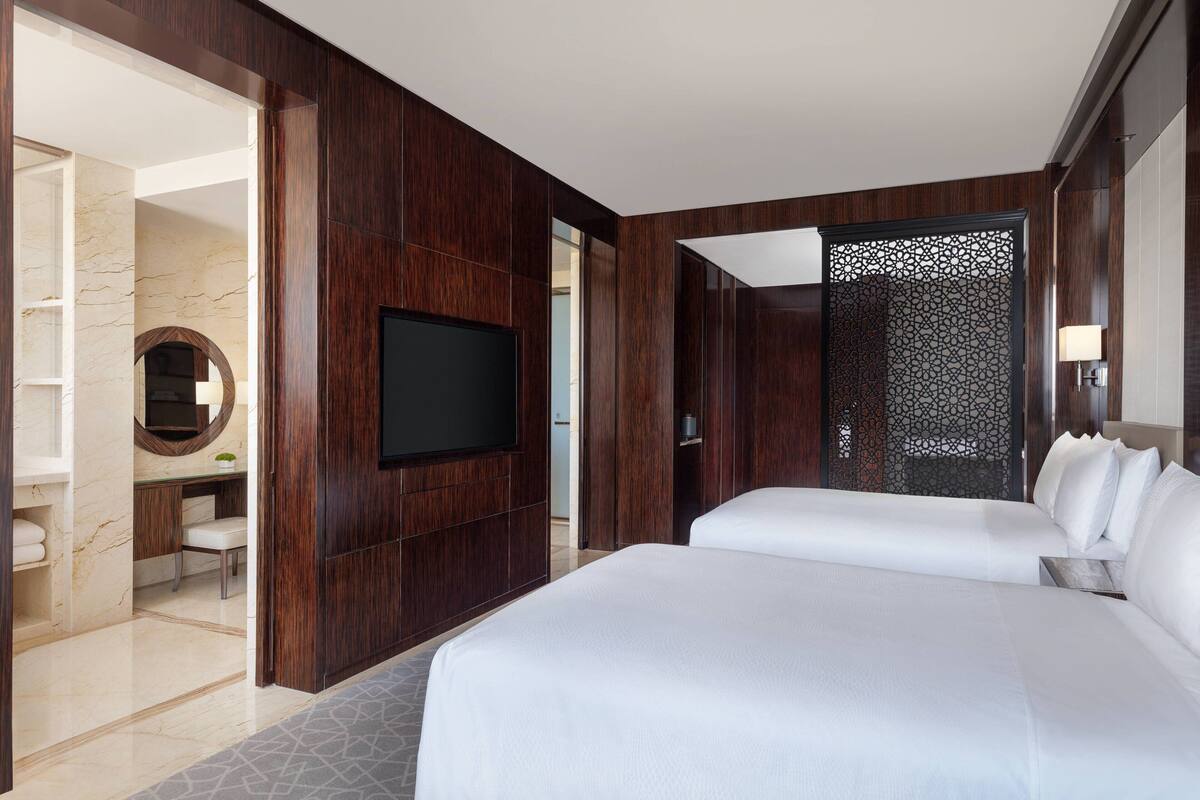 Une chambre d’hôtel moderne dotée d’un grand lit, d’une télévision à écran plat, d’un bureau avec une chaise et d’une salle de bain avec un mur et un lavabo en marbre.