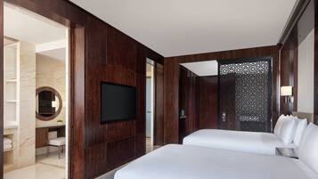 A modern hotel room with a large bed, a flat-screen TV, a desk with a chair, and a bathroom with a marble wall and sink.
