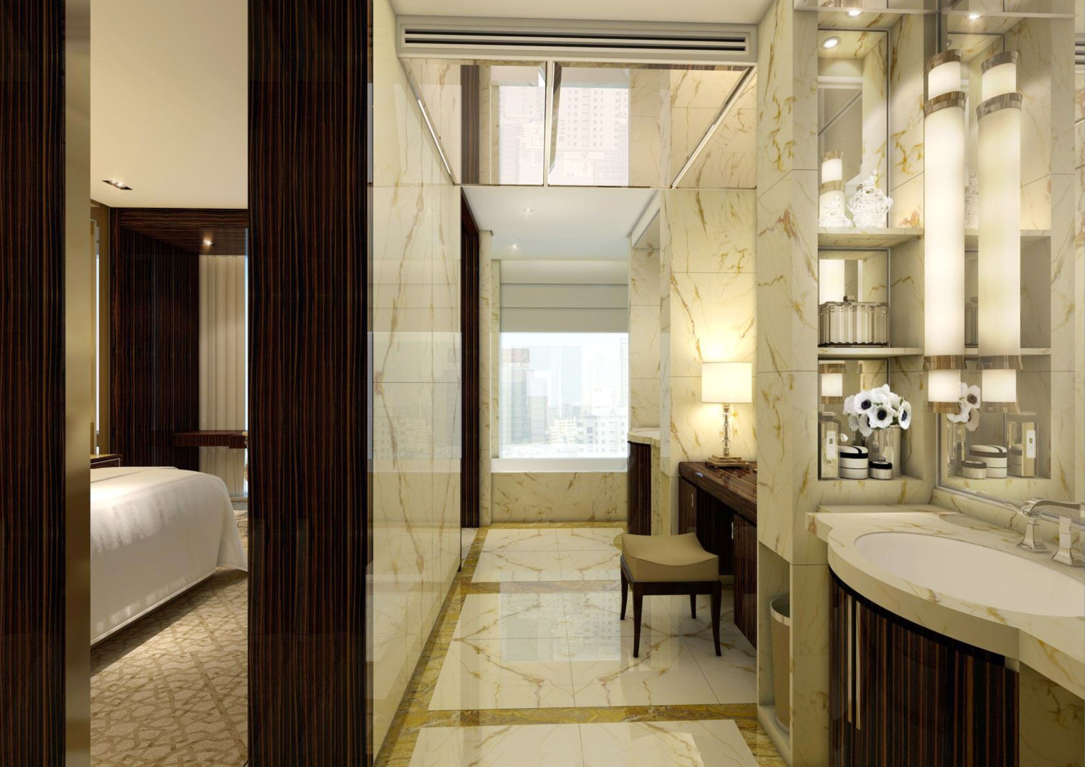 A modern hotel bathroom with a large mirror, two sinks, a vanity, and a chair.