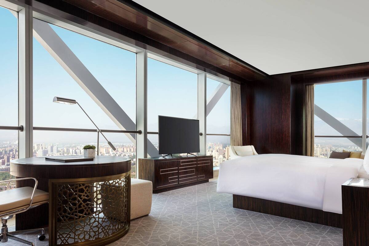 Une chambre d’hôtel située dans un immeuble de grande hauteur, offrant une vue sur la ville, avec un grand lit, un bureau avec une chaise, une télévision et un meuble décoratif.