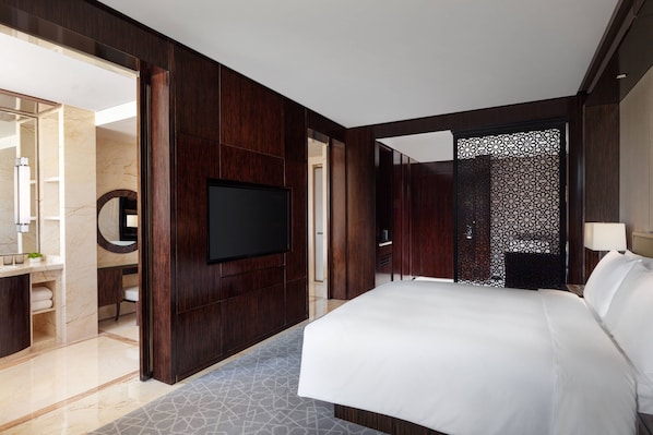 Een moderne hotelkamer met een groot bed, een flatscreen-tv, een badkamer met spiegel en wastafel, en een decoratief wandpaneel.