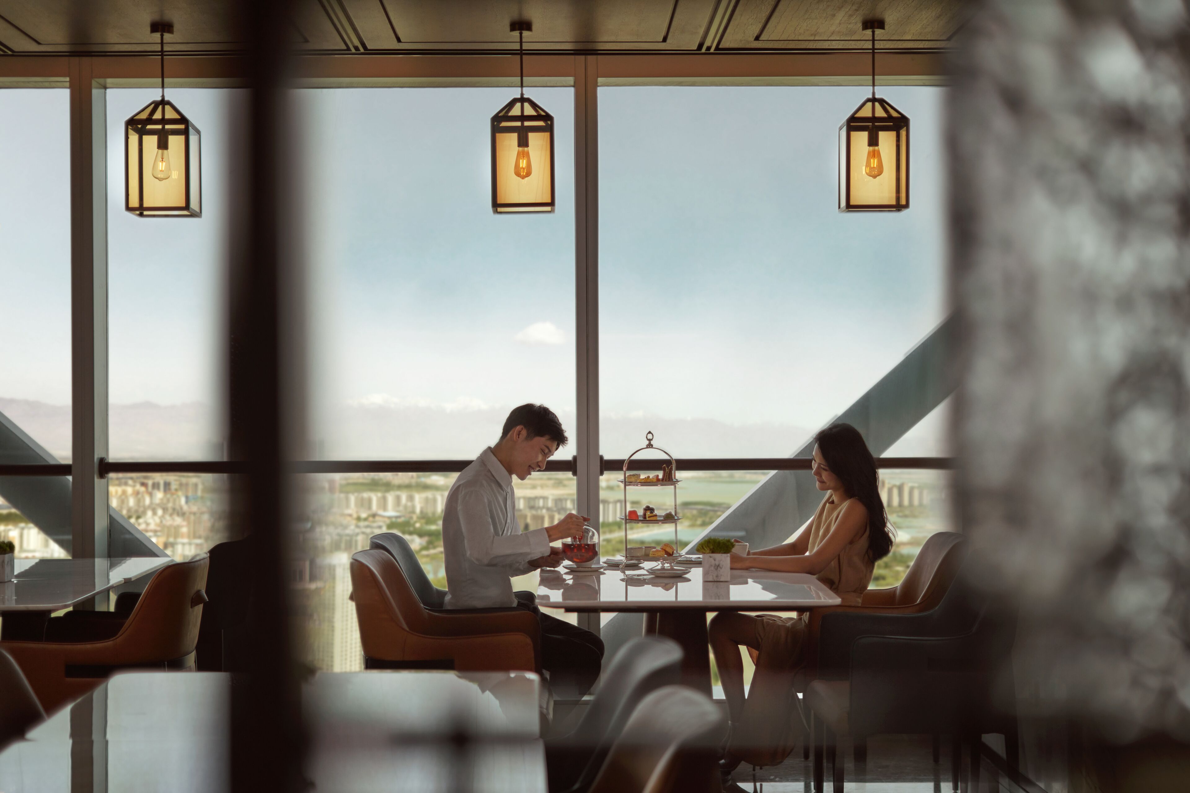 Uma área de jantar moderna com uma mesa posta para dois, grandes janelas com vista e iluminação pendente.