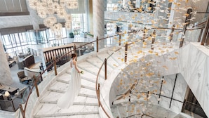 Una imponente escalera de mármol con barandas de cristal, que conduce a un nivel inferior con asientos y vistas del vestíbulo.