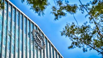 Een modern gebouw met een opvallend logo op de gevel, grote ramen en een helderblauwe lucht op de achtergrond.