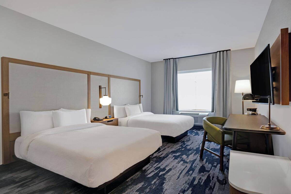 A hotel room with two beds, a desk with a chair, a TV, and a window with curtains.