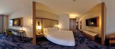 A hotel room with a large bed, a desk, a chair, a TV, and a bathroom.