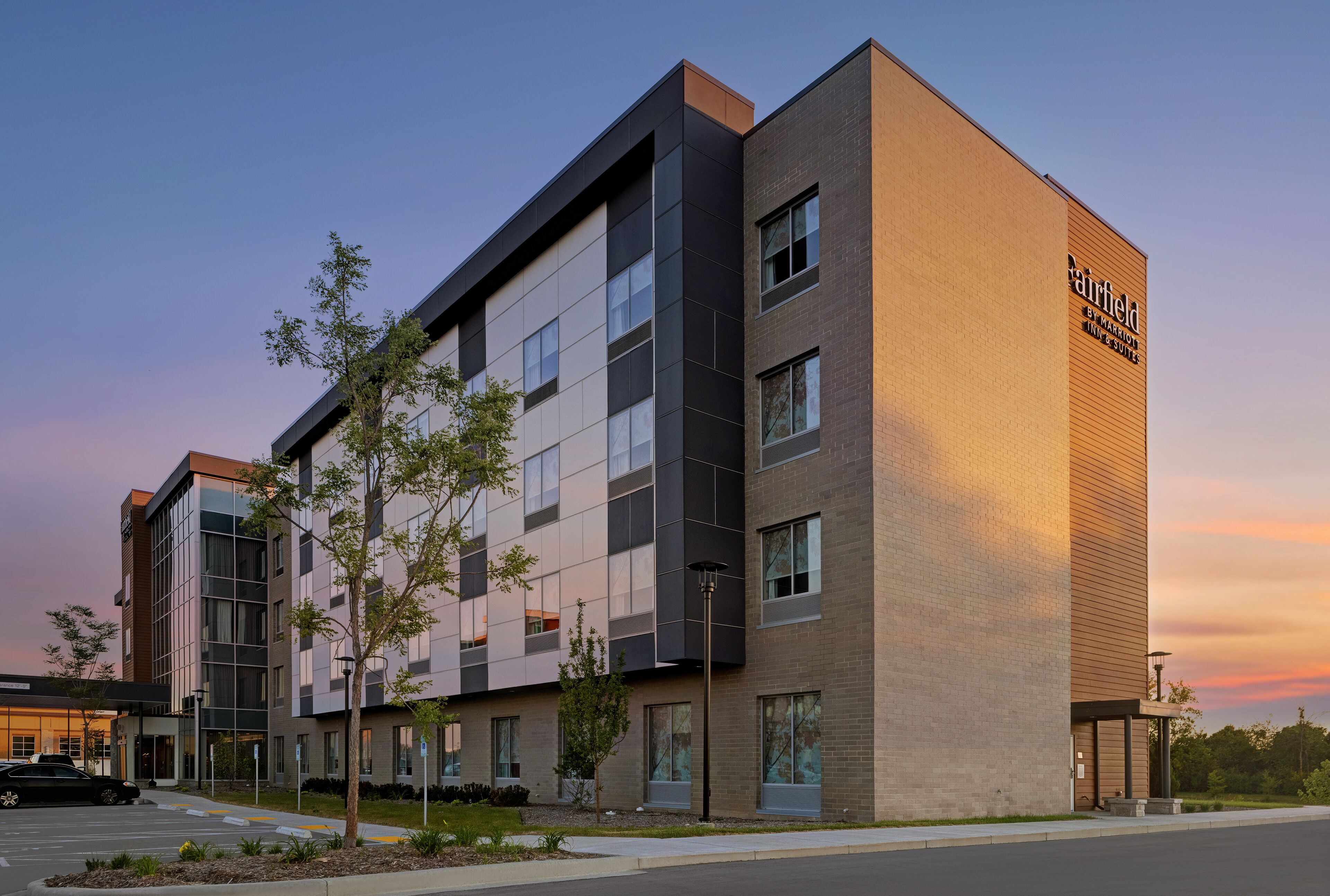 Un hôtel moderne, avec une façade combinant verre et briques, de nombreuses fenêtres et un parking.