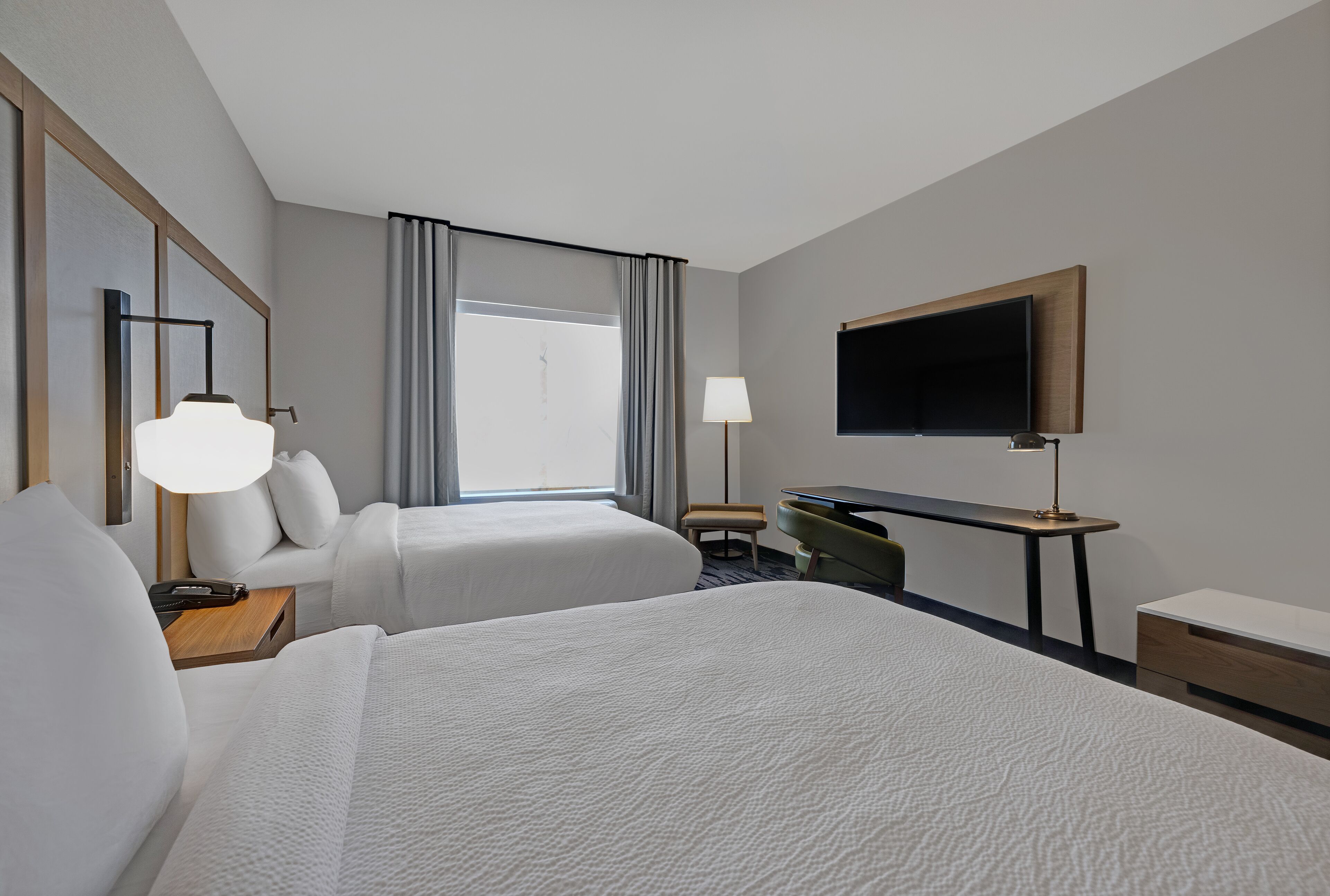 Une chambre d’hôtel avec deux lits, un bureau, une télévision et une fenêtre avec des rideaux.