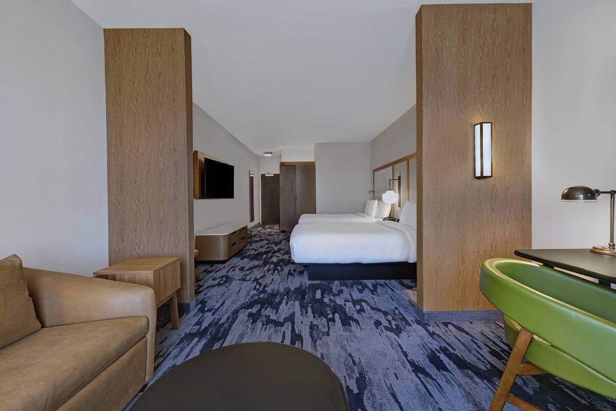 A hotel room with a large bed, a green chair, a desk, and a sofa.