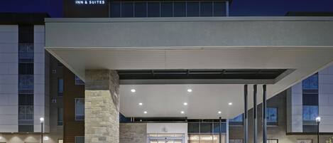 A modern hotel entrance with a marquee sign, a covered walkway, and a well-lit facade.