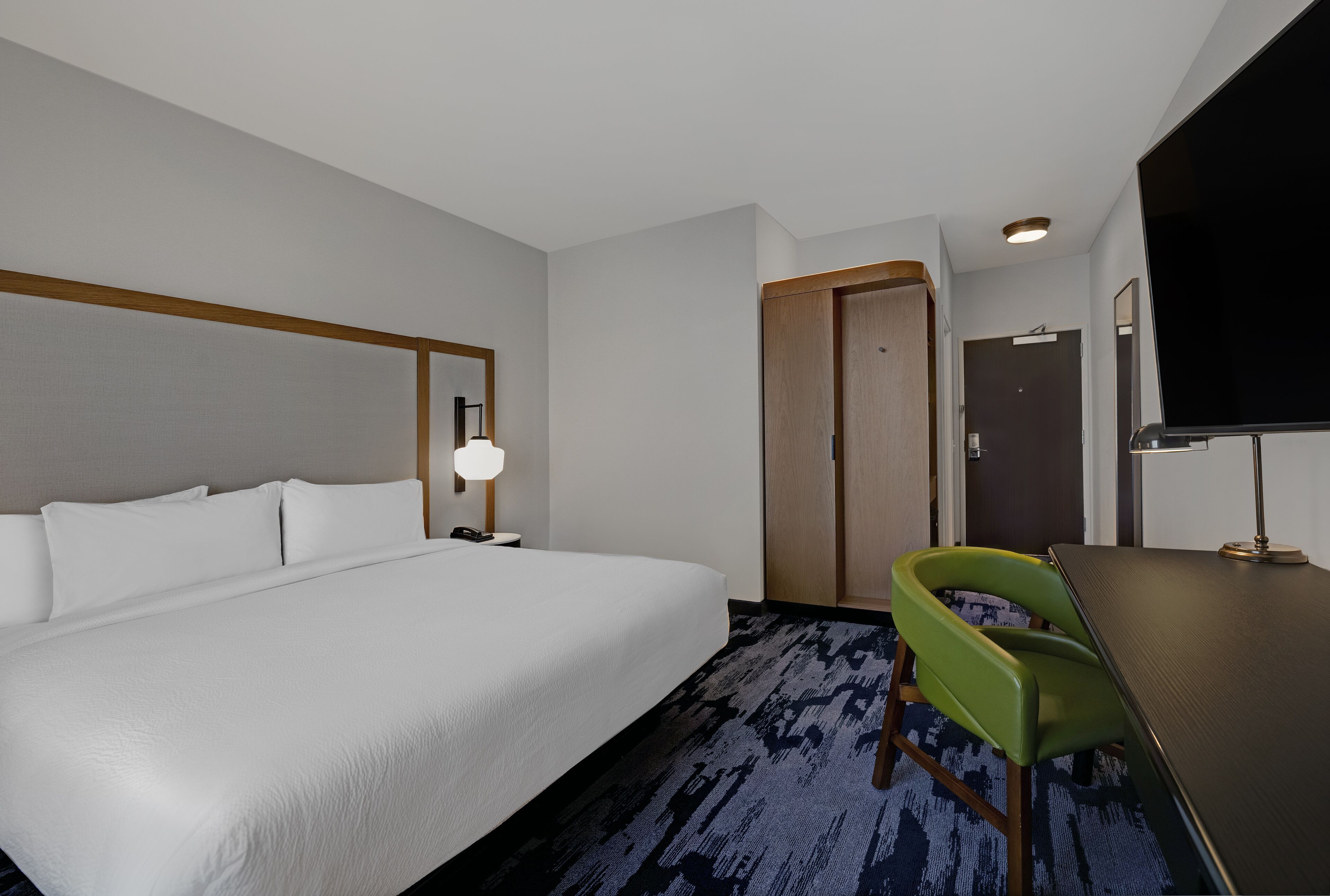 Ein Hotelzimmer mit einem großen Bett, einem Schreibtisch mit Stuhl, einem Fernseher und einer Tür.