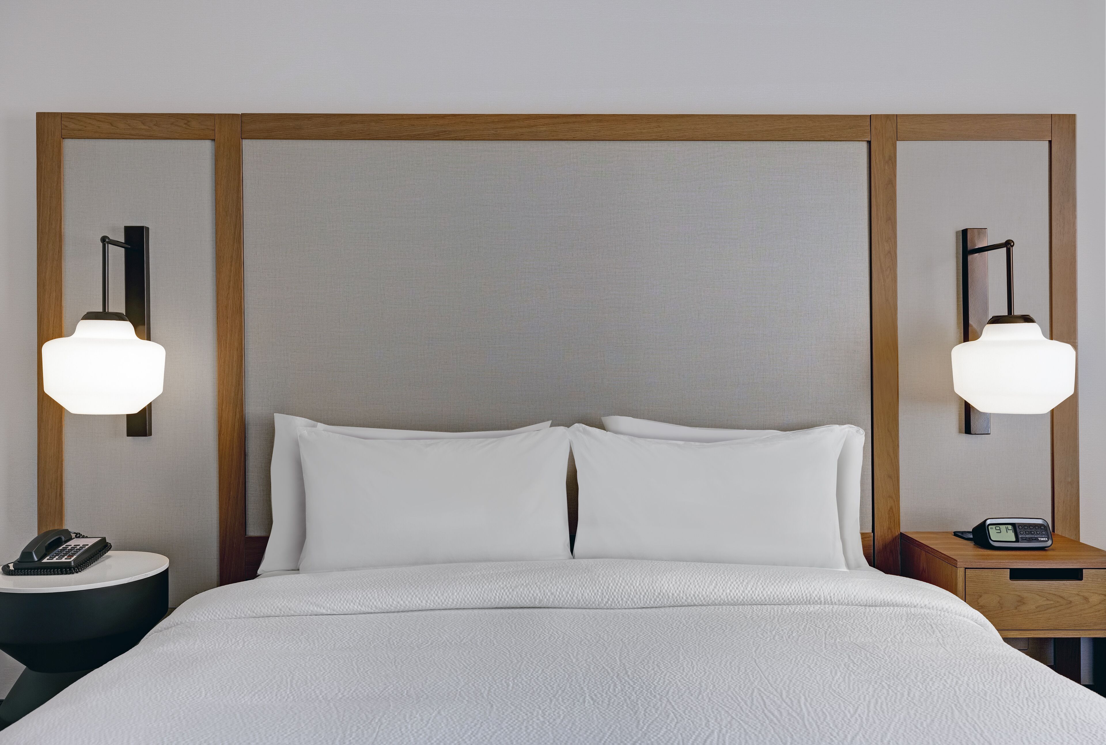 Une chambre d’hôtel avec un grand lit, deux tables de chevet, une petite table et une lampe fixée au mur.