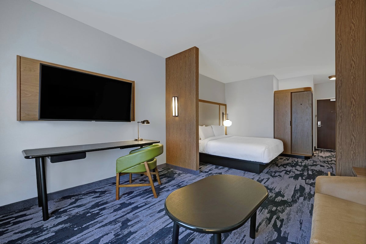 A hotel room with a bed, a desk, a chair, a TV, and a lamp.