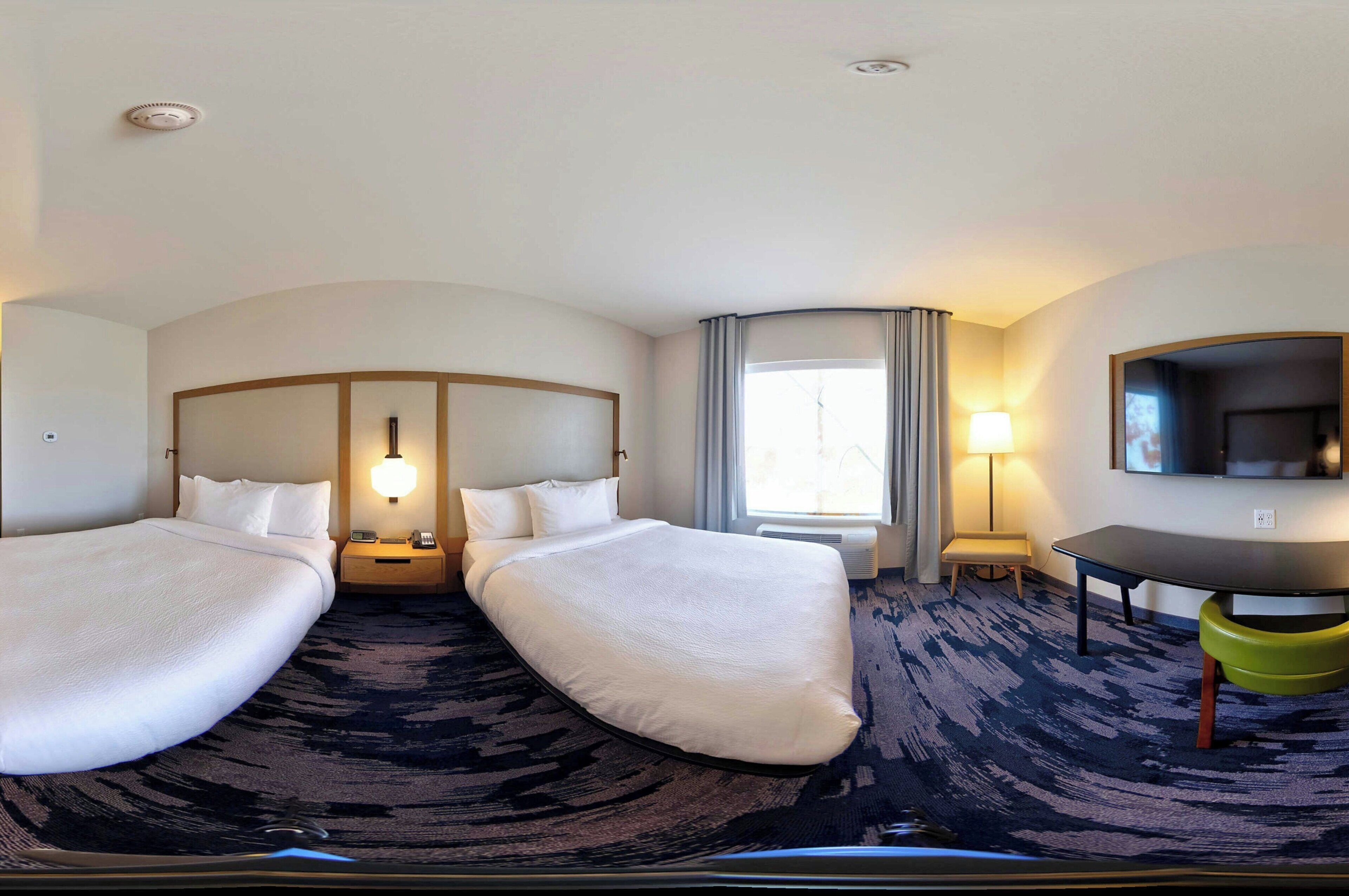 Habitación de hotel con dos camas, un escritorio, un televisor y una ventana con cortinas.