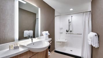 A modern bathroom with a large sink, mirror, shower, and towel rack.