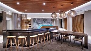 Uma área de bar moderna com banquetas de madeira, uma mesa comprida e luminárias pendentes.