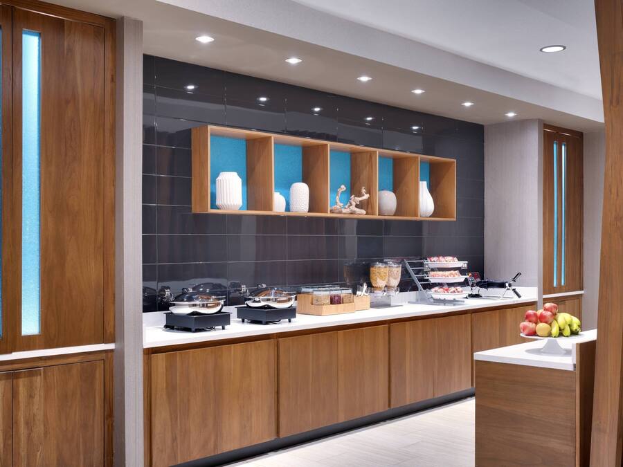 A modern kitchen with wooden cabinets, a black backsplash, and a variety of food items displayed on the counter.