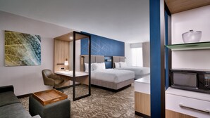 Quarto de hotel com cama, escrivaninha, cadeira, micro-ondas e pequena área de refeições.