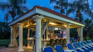 Ein überdachter Außenbereich mit Bar, Lounge-Stühlen und Palmen im Hintergrund.
