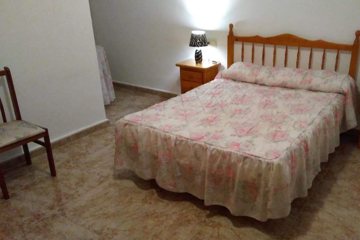 A bedroom with a bed, a nightstand, a chair, and a lamp.