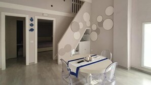 A modern dining area with a white table and chairs, a staircase with circular wall decorations, and a view of a room with a wardrobe. - Casa Bolle (Sicilia)