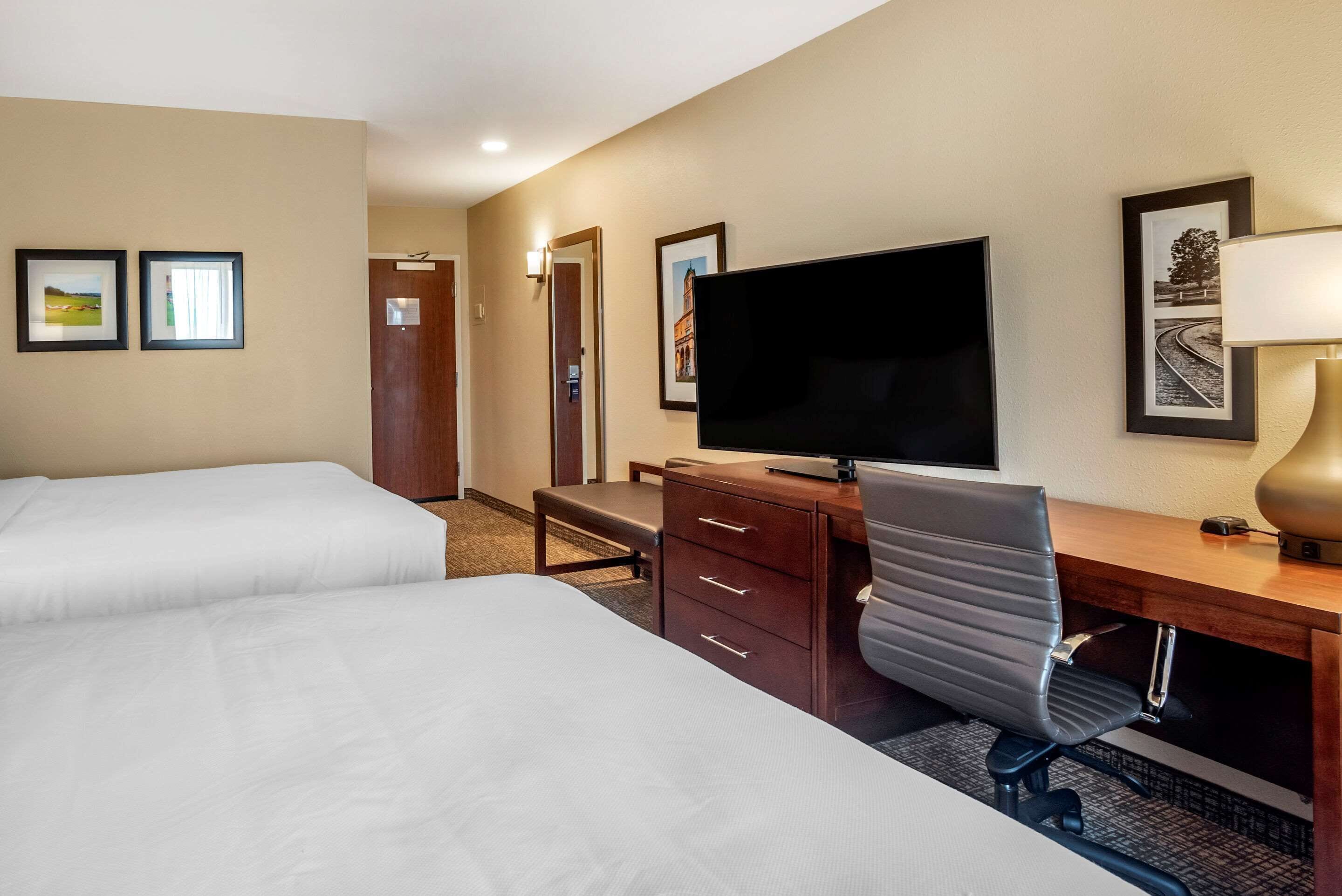A hotel room with two beds, a desk with a computer, a TV, and a lamp.