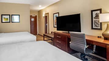 A hotel room with two beds, a desk with a computer, a TV, and a lamp.