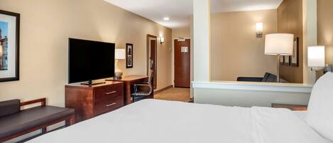 Habitación de hotel con una cama grande, un televisor de pantalla plana, un escritorio con silla, un espejo y una puerta que da a otra habitación.