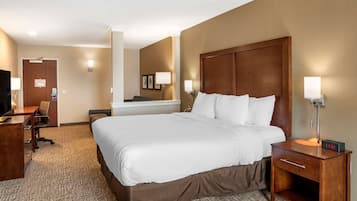 A hotel room with a large bed, a desk with a chair, a TV, and a small table with a lamp.