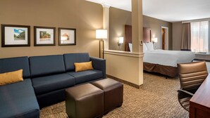 A hotel room with a sofa, ottoman, bed, and a desk. There are framed pictures on the wall and a lamp near the bed. - Comfort Inn & Suites Harrisonburg (Harrisonburg)