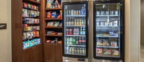 Una estación de bebidas autoservicio con dispensadores refrigerados y estantes con aperitivos.