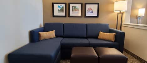 Un salon moderne avec un canapé d’angle, un pouf assorti et trois tableaux encadrés accrochés au mur.