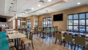 A spacious hotel dining area with multiple tables and chairs, a flat-screen TV mounted on the wall, and large windows providing a view of the parking lot. - Comfort Inn & Suites Harrisonburg (Harrisonburg)