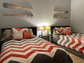 Habitación de hotel con dos camas, cada una con una colcha estampada y varias almohadas. Dos palas de madera están sujetas a la pared sobre las camas.