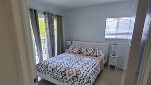 Ein Schlafzimmer mit einem Bett, einem Nachttisch, einem Fenster mit Jalousien und einer Tür.