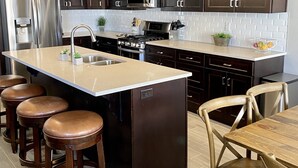A modern kitchen with dark wood cabinets, stainless steel appliances, and a central island with stools. - NEW🌟Spacious, Zion Village 7BD/6BA, Sleeps 32, Pool, Lazy River, View  (Hurricane)
